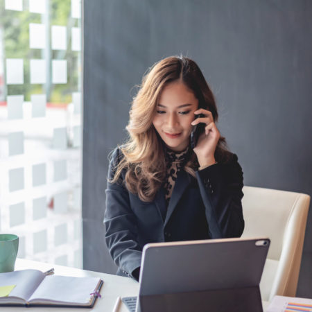 Happy young asian woman talking on the mobile phone and smiling while sitting at her working place in office.