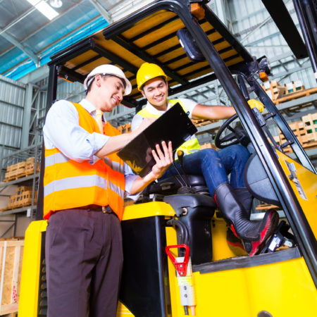 Asian fork lift truck driver discussing checklist with foreman in warehouse